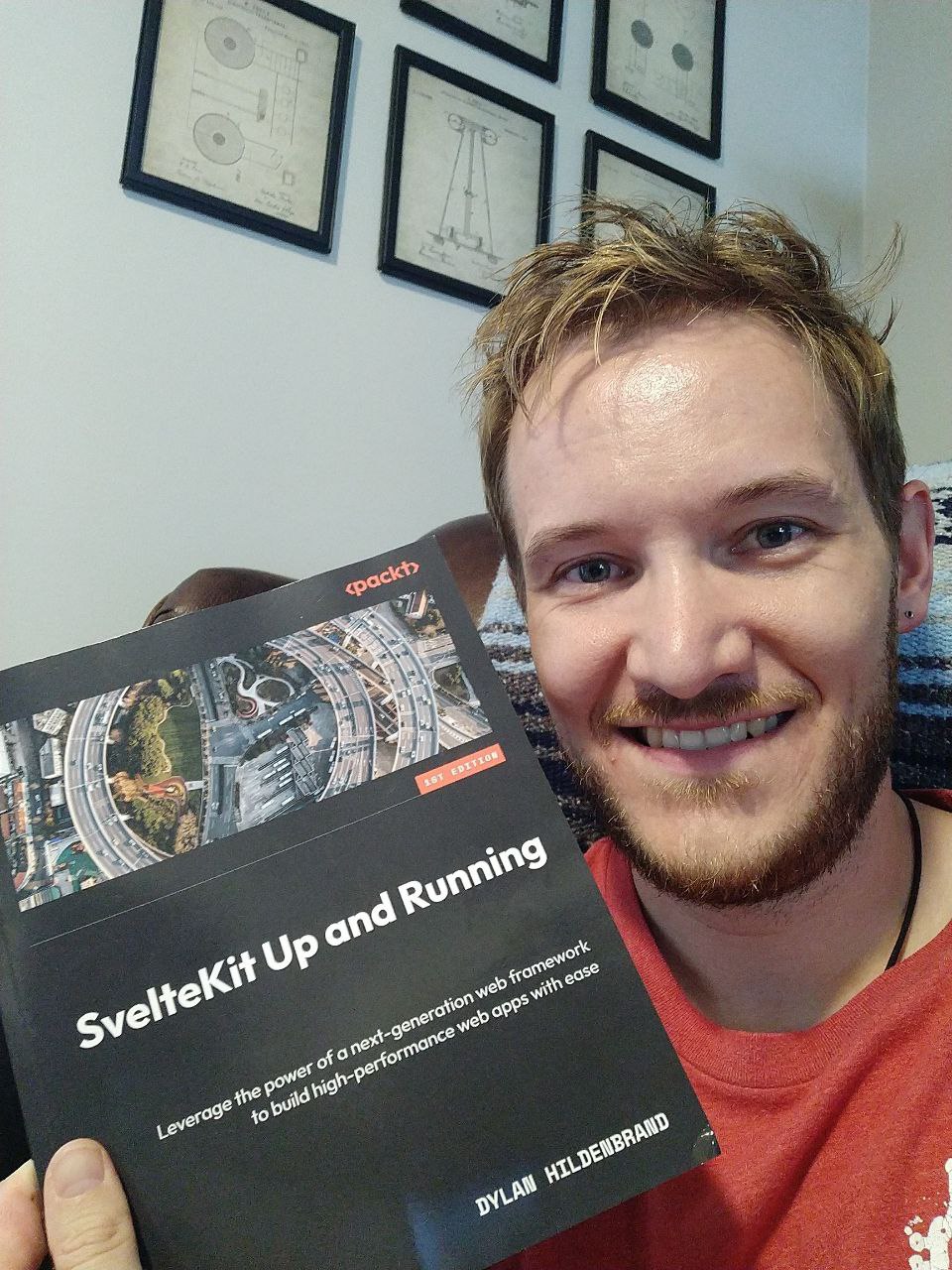 Author of the book SvelteKit Up and Running, Dylan Hildenbrand (that's me!) poses with a copy of his book in hand while smiling.